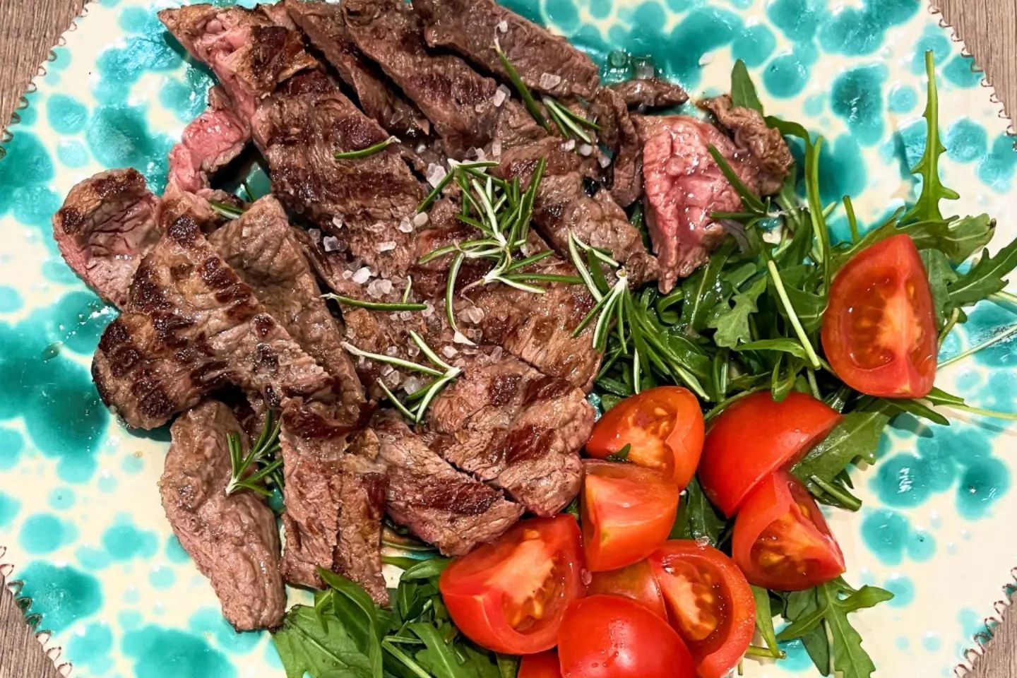 Tagliata di carne alla brace con rucola e pomodorini su piatto in ceramica decorata